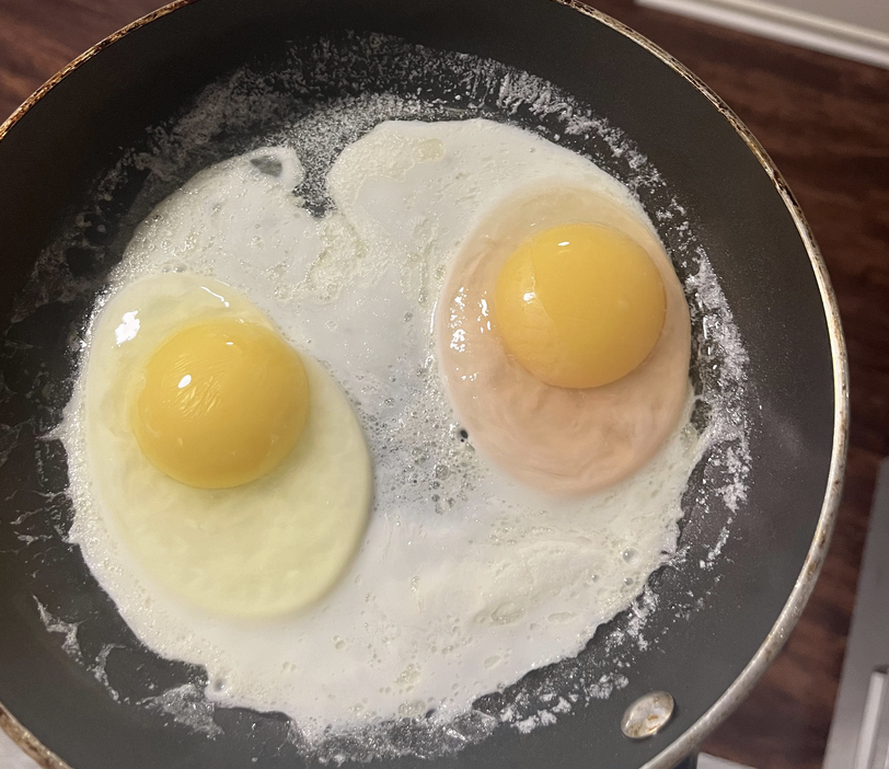 two eggs in a frying pan with one having pink white part